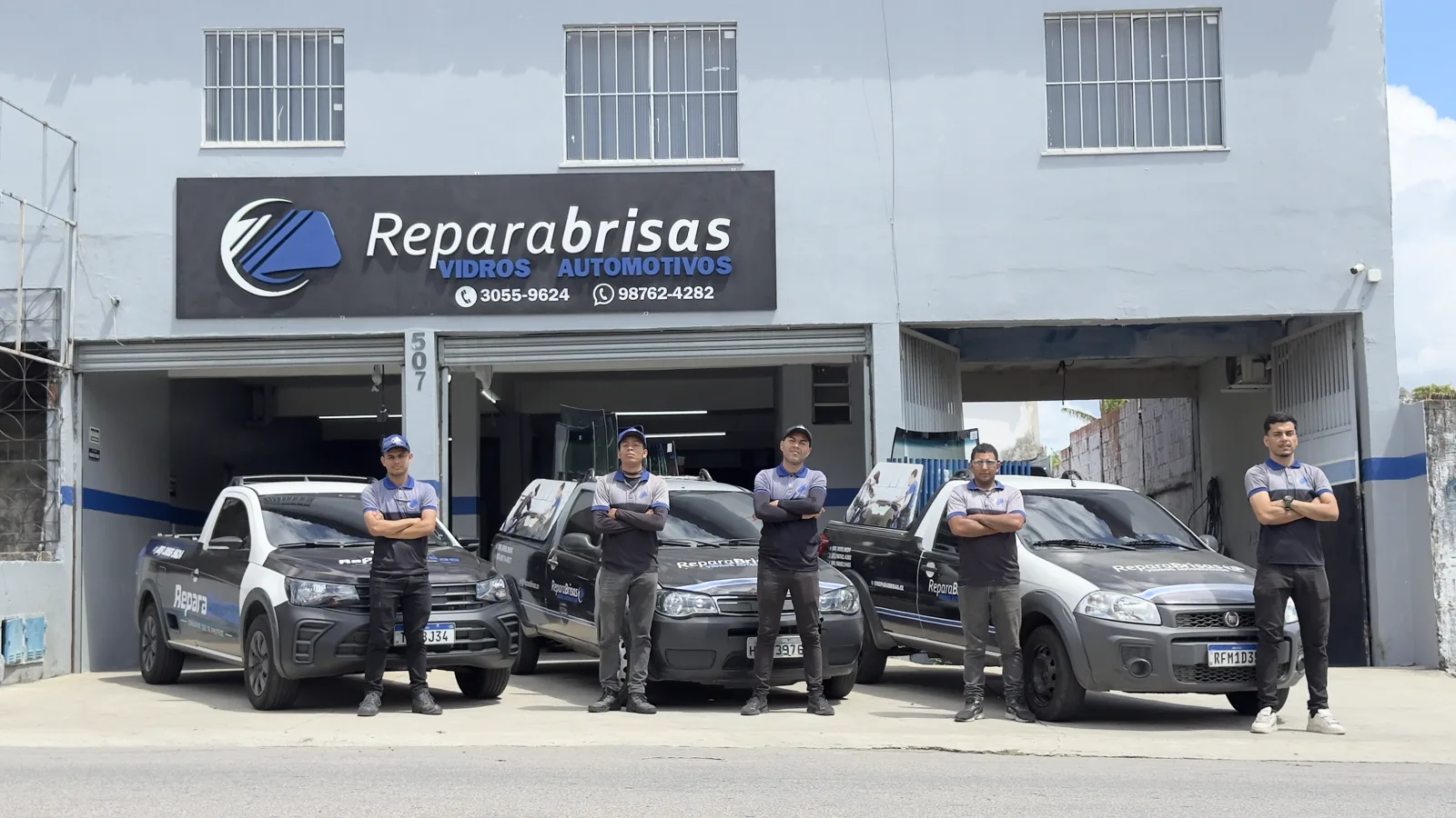 Equipe da ReparaBrisas de uniforme em frente à loja, com a frota de atendimento